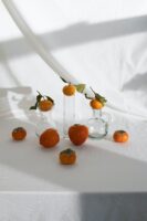 composition of mandarins and persimmon placed on white table with glassware